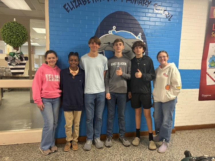 Six members of the East Bladen High School Student Government stand together in front of the Elizabethtown Primary School dolphin mural inside the school. They are visiting to read to EPS students and support literacy.