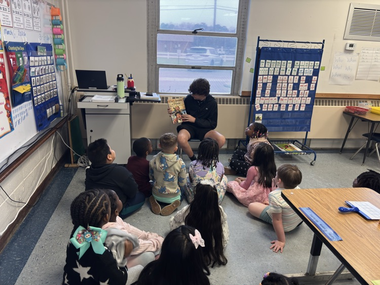 students sit in crisscross on the floor ETP listening to a story be told by a student in a black shirt