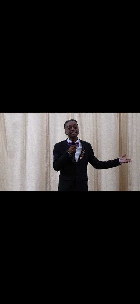 student in a Sutton stage with a gold background with his hand, stuck out giving a speech