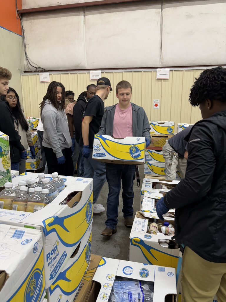 A group of West Bladen High School students volunteer together, packing yellow boxes with food at a community food bank