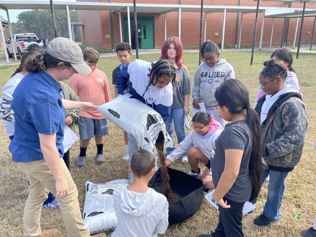 An instructor pours soil from a bag into a large container while a group of students watch and prepare for a hands-on soil study activity.