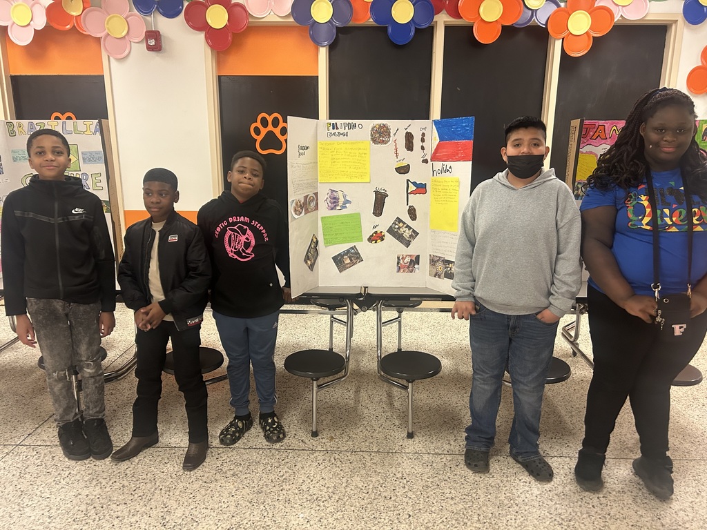 Five students stand with a Filipino culture presentation board featuring the Philippines flag, traditional foods, holidays, and cultural customs.
