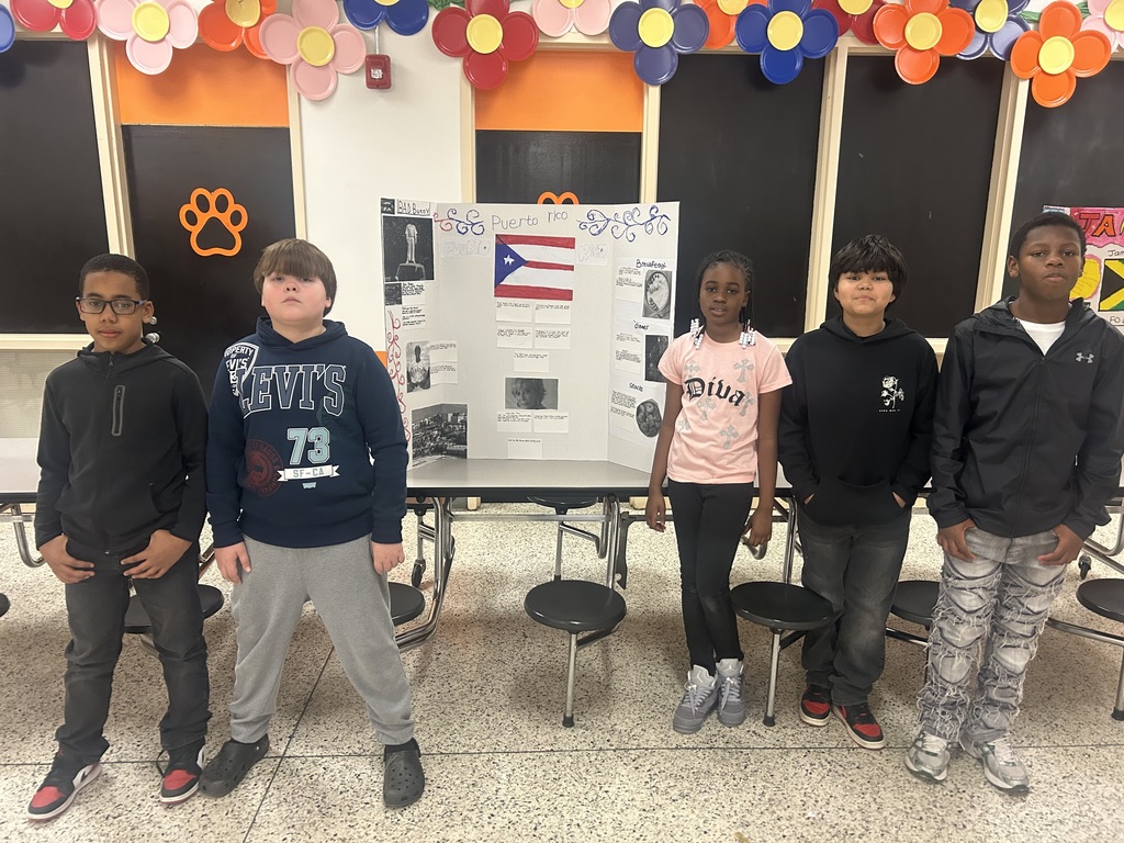 Six students stand beside a tri-fold display about Puerto Rico, featuring the Puerto Rican flag and information about culture, food, and important landmarks during the ETMS Multicultural Celebration.
