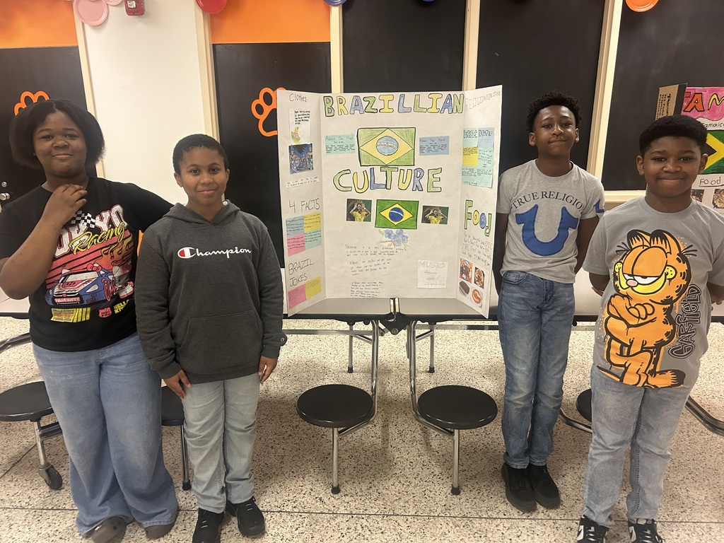 Four students present a colorful Brazilian Culture project board that includes the Brazilian flag, facts about the country, music, food, and cultural traditions.