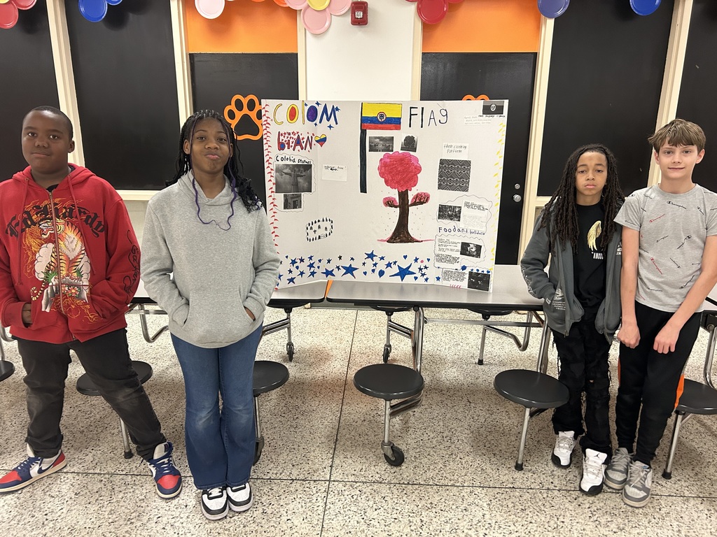 Five students pose with a Colombia culture project board showing the Colombian flag, landmarks, food, and cultural facts.