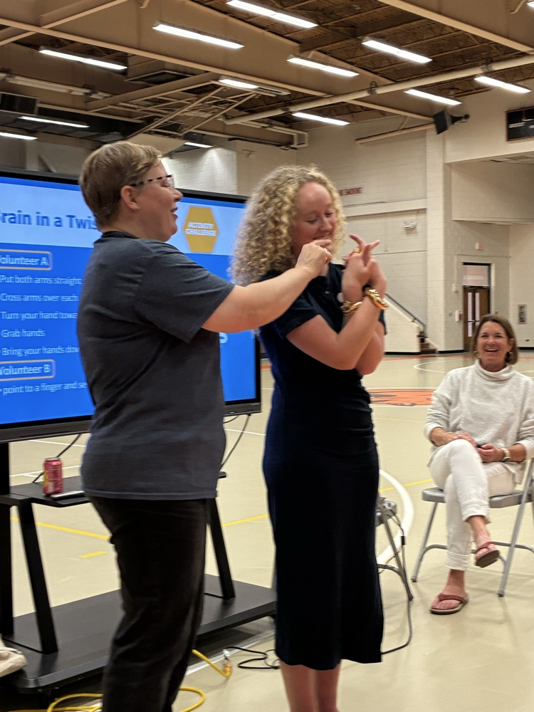 two ladies standing next to each other doing an arm activity and one lady sitting in a chair