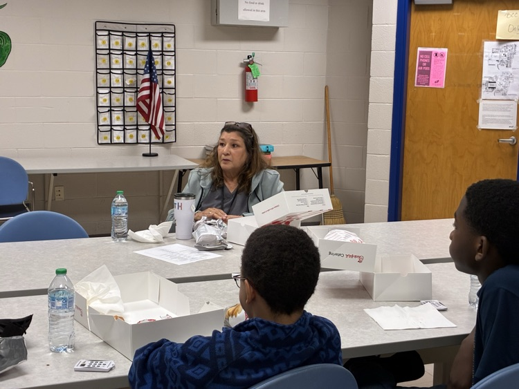 teacher and two students eating dinner at tables listening to presenter