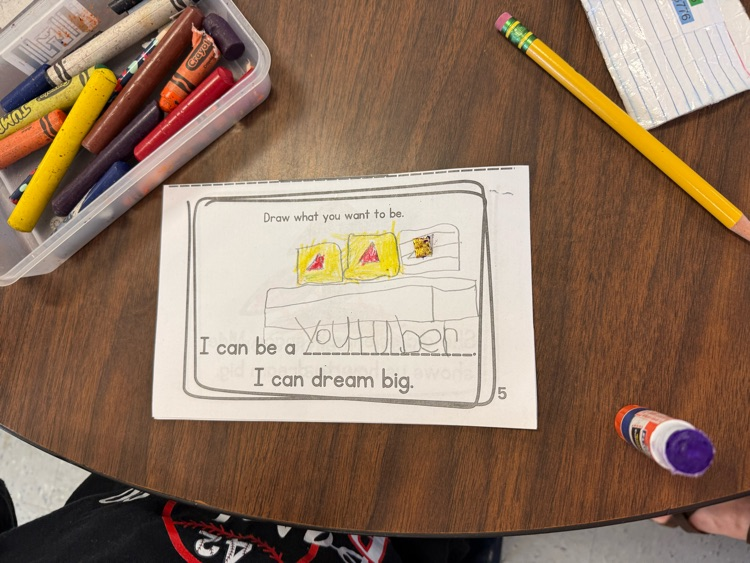 Student worksheet showing a drawing of a YouTuber with screens and a desk, with crayons nearby.