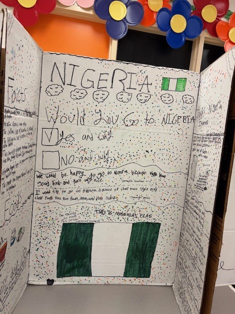 Student project board about Nigeria displaying the Nigerian flag and written responses explaining why someone might want to visit Nigeria.