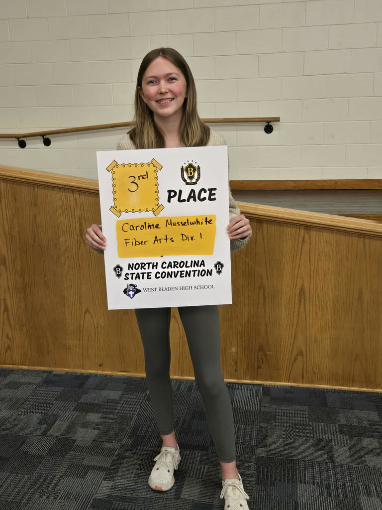 West Bladen High School student holds a "Premier Performers" award certificate while standing inside a school building