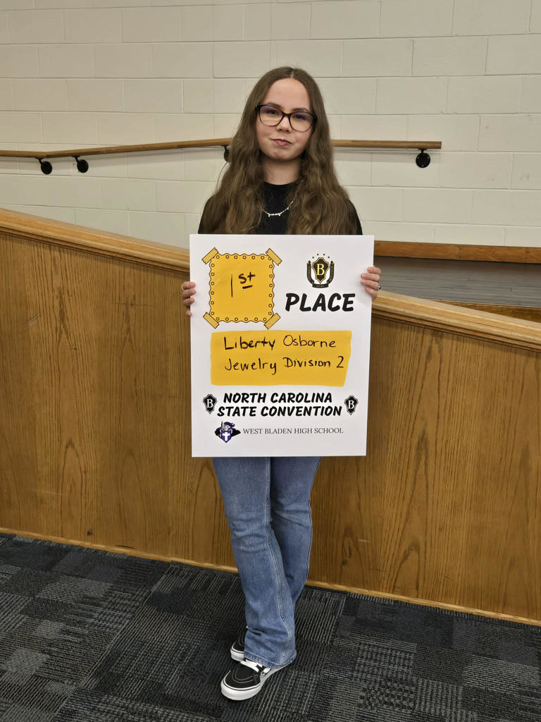 West Bladen High School student holds a "Premier Performers" award certificate while standing inside a school building
