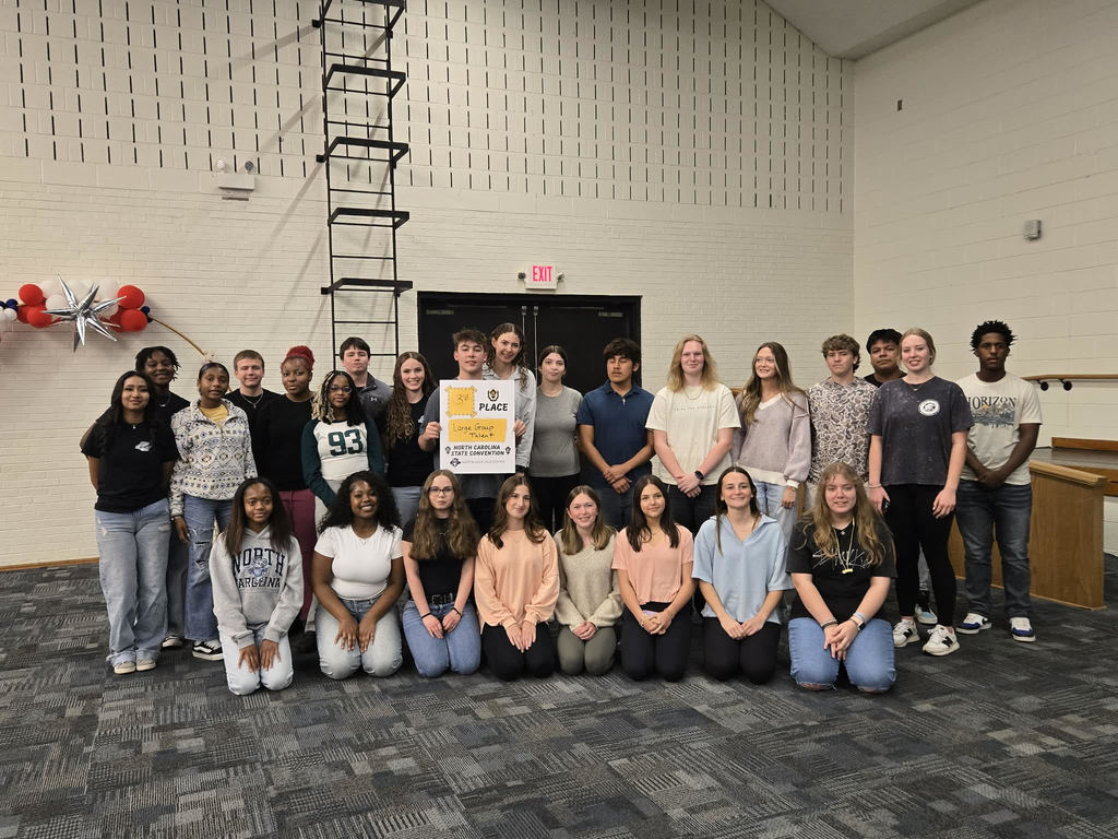 A group of approximately 25 high school students and two teachers pose together indoors. A student in the center holds a yellow "2nd Place" award certificate from a North Carolina convention
