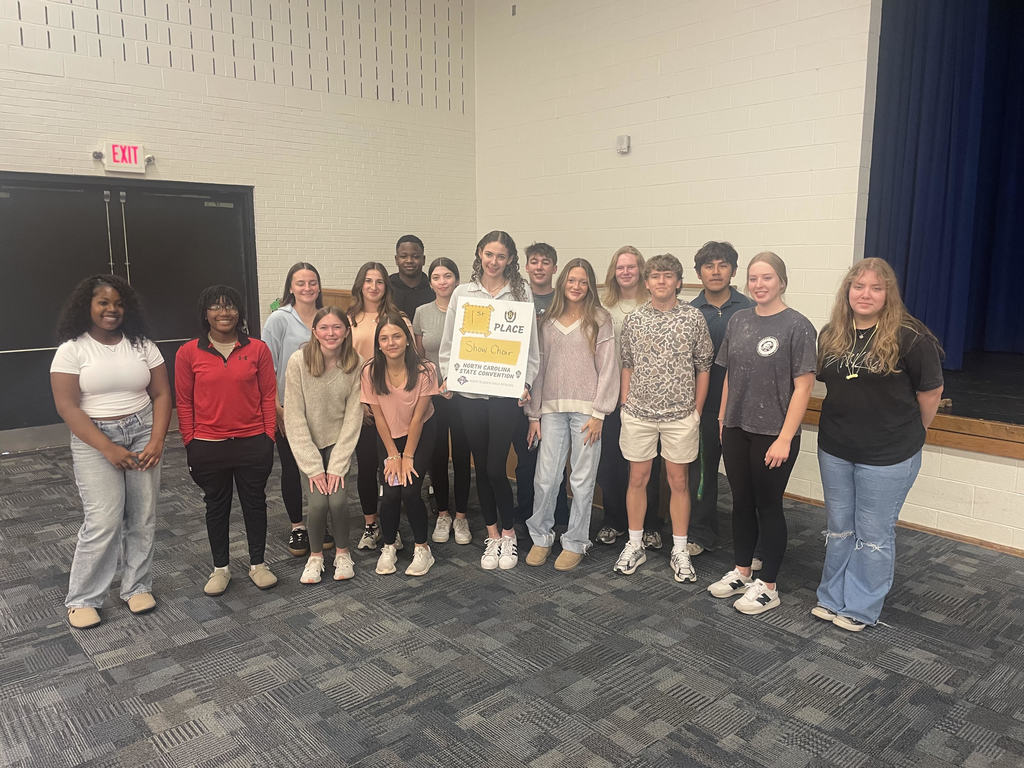 Group of West Bladen High School students standing in a gym, smiling and holding a yellow award plaque for their Show Choir performance at a state convention