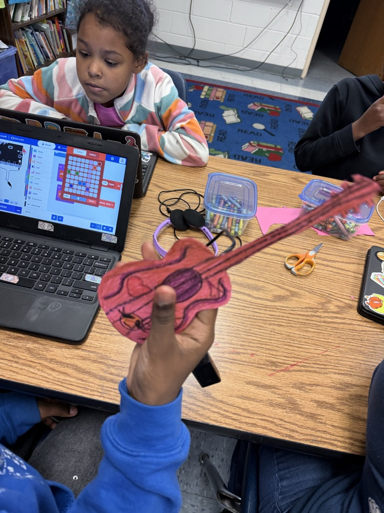 Student holding up a completed paper guitar with a micro:bit attached, demonstrating their finished STEM project