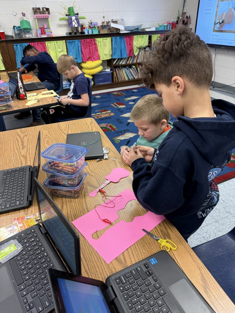 . Close-up of a student connecting a micro:bit to a paper guitar while coding on a laptop screen