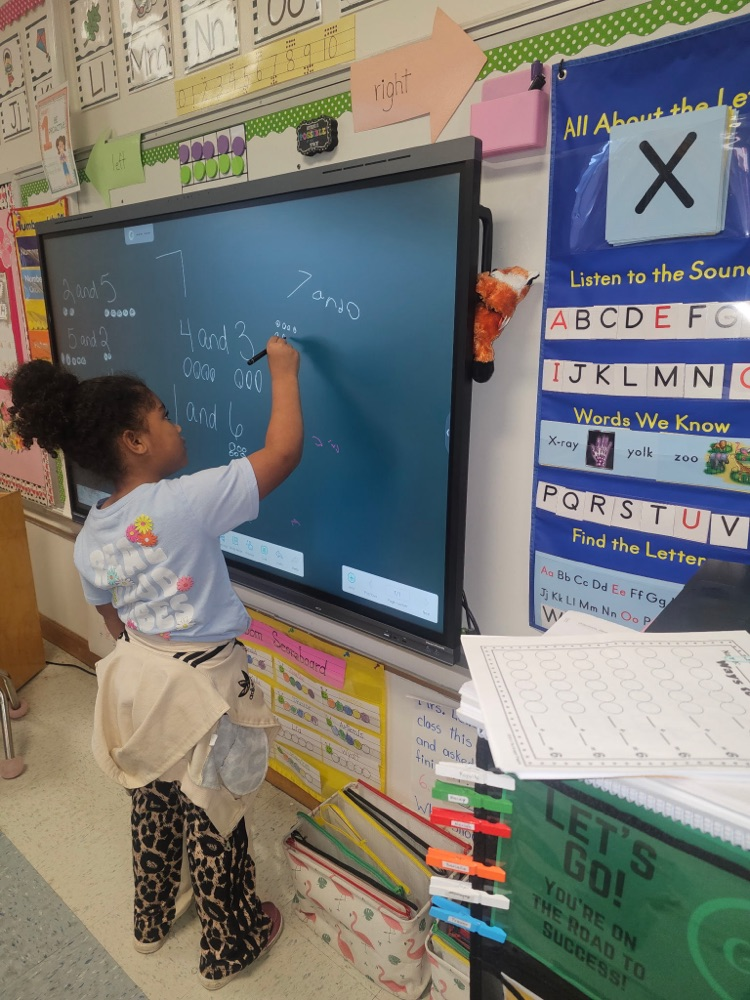 A student uses a stylus on a large digital board to solve composing and decomposing number problems, showing combinations that make 7 with drawn dots.