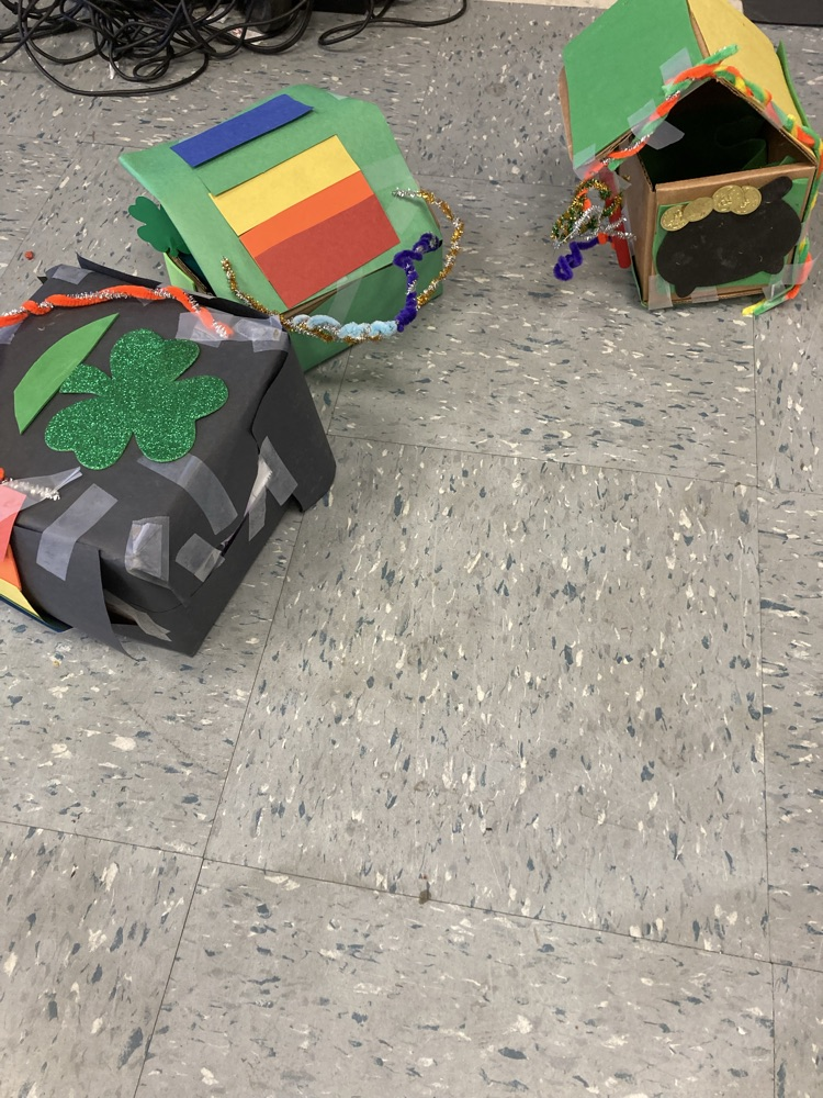 Completed leprechaun traps sit on the classroom floor, decorated with shamrocks, bright colors, and pipe cleaners, ready to catch a leprechaun.