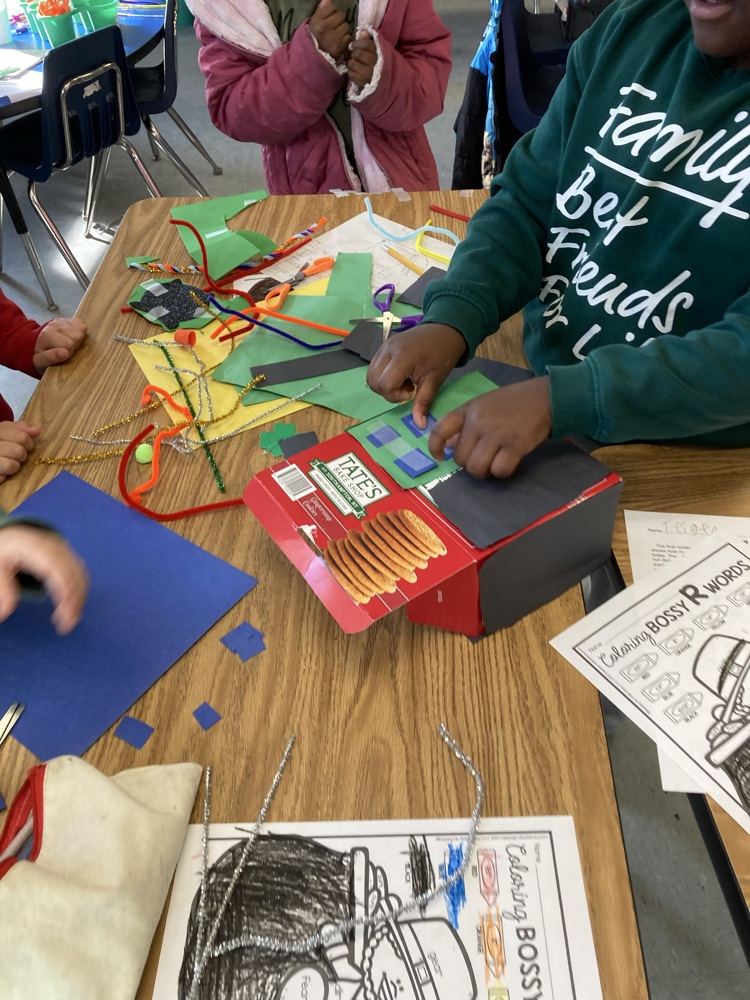 Close-up of a student decorating a cardboard box trap with paper shapes and craft materials as part of a group STEM activity.