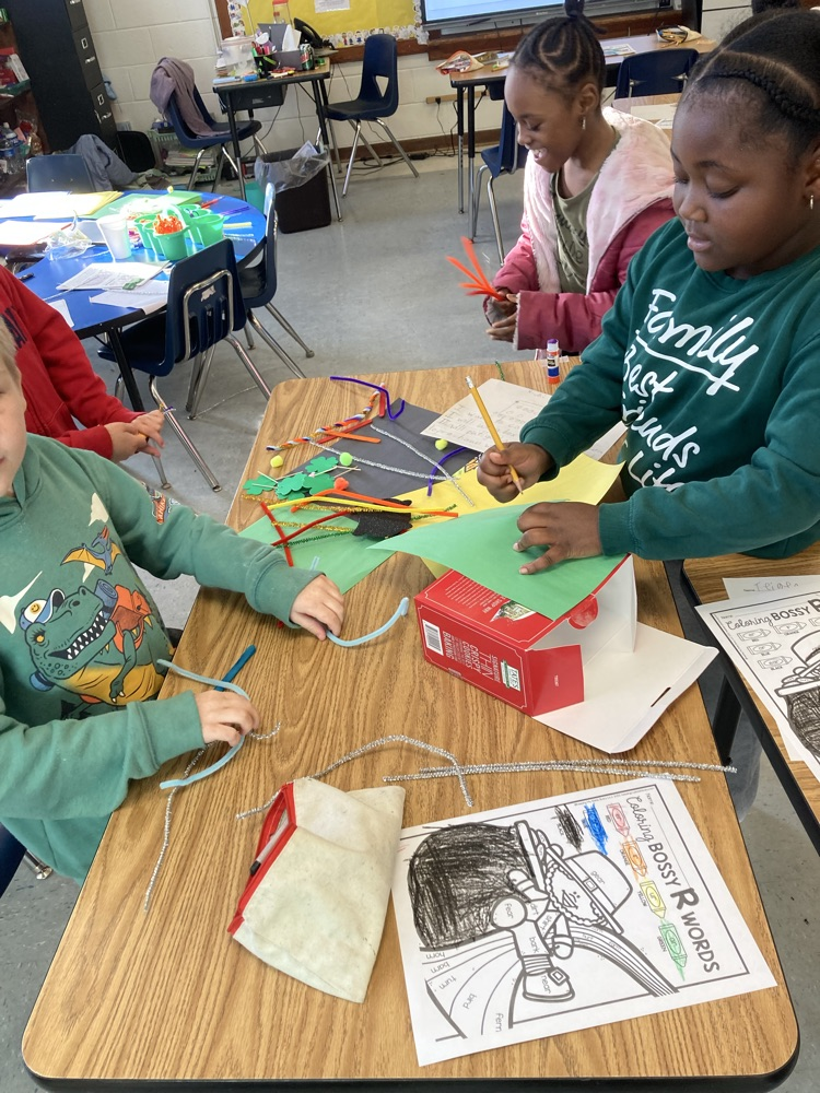 Students sit together at a table building their trap using a cardboard box, pipe cleaners, and colorful materials while collaborating and sharing ideas.