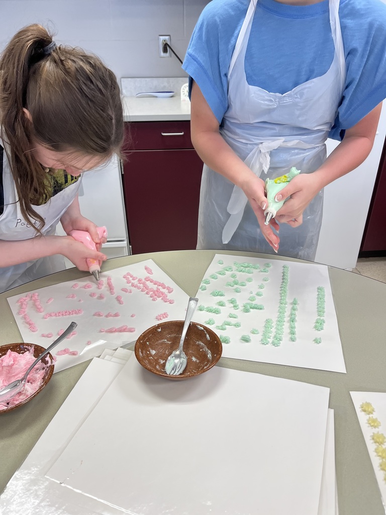 Two students wearing white aprons and blue shirts work together to decorate a pastry with yellow frosting