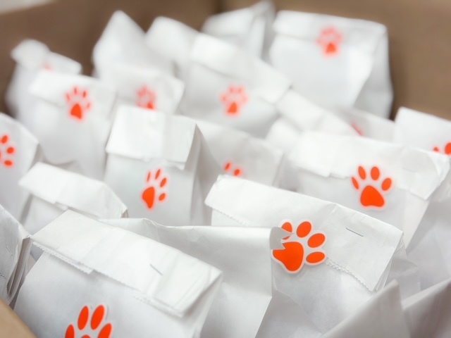 A box filled with small white treat bags, each decorated with a bright orange paw print sticker.