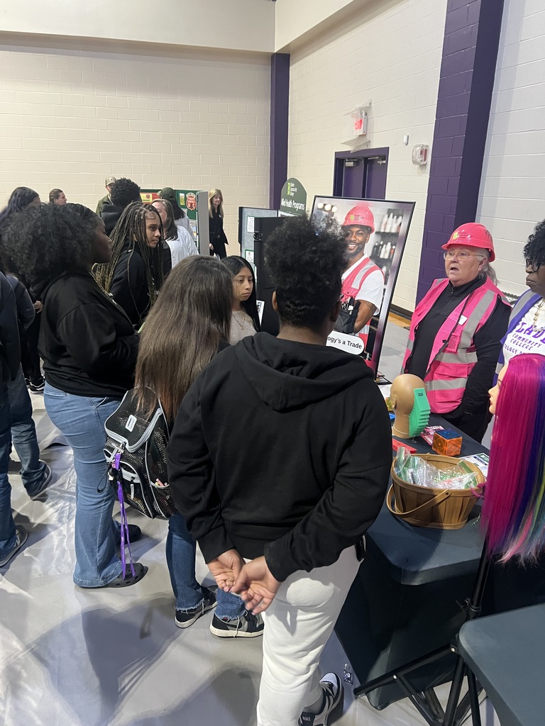 Students at a career fair booth looking at a purple-haired mannequin and a basket of samples at a trade display