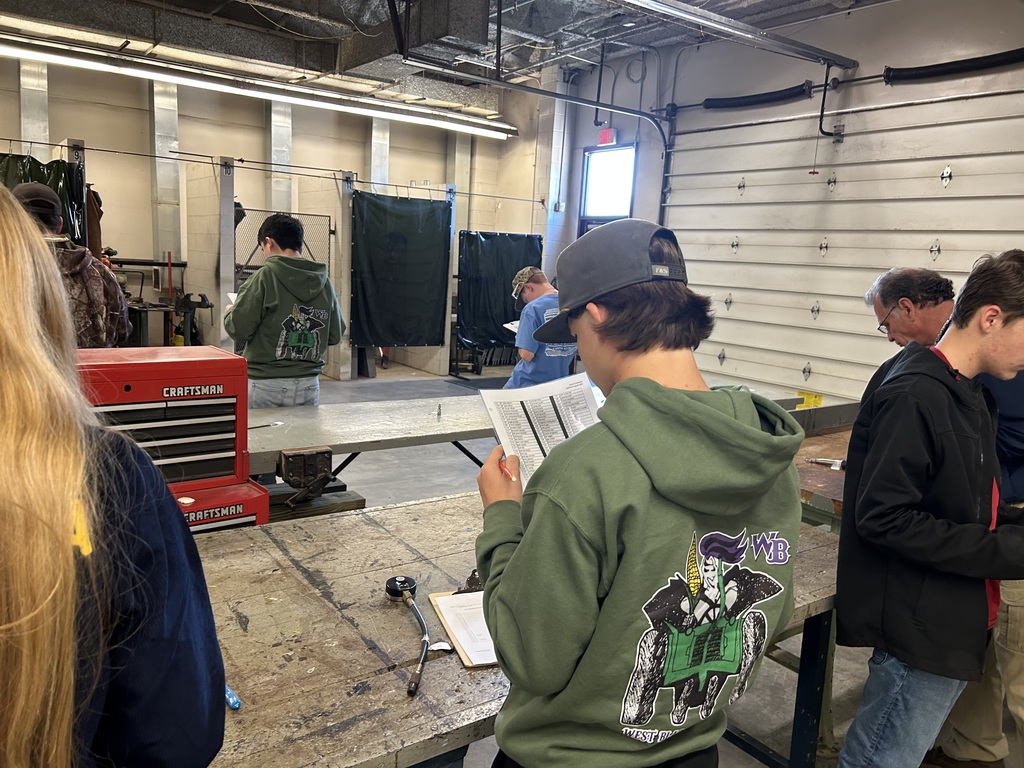 Students in an agricultural shop looking at a manual near a red Craftsman toolbox and welding stations