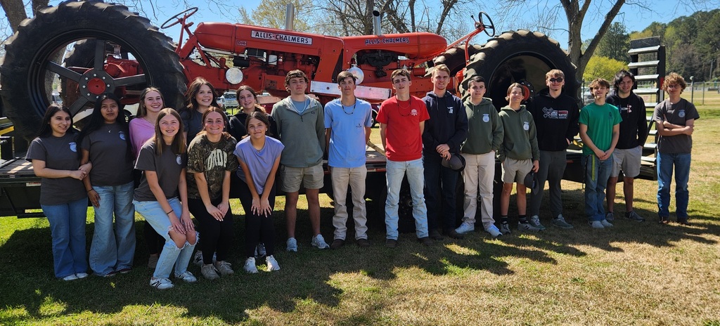 A group of West Bladen FFA students poses in front of a large orange antique tractor on a sunny day in a grassy field