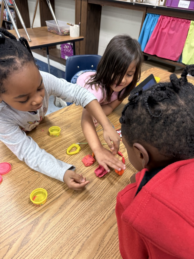 Young students work together at a table using Play-Doh and Makey Makey to build circuits and experiment with sound on a laptop.