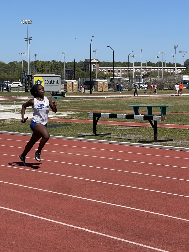 Female student in track uniform running on a track with a baton in their hand.