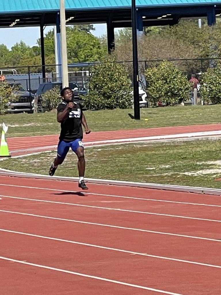Male student in track uniform running on a track with a baton in their hand.