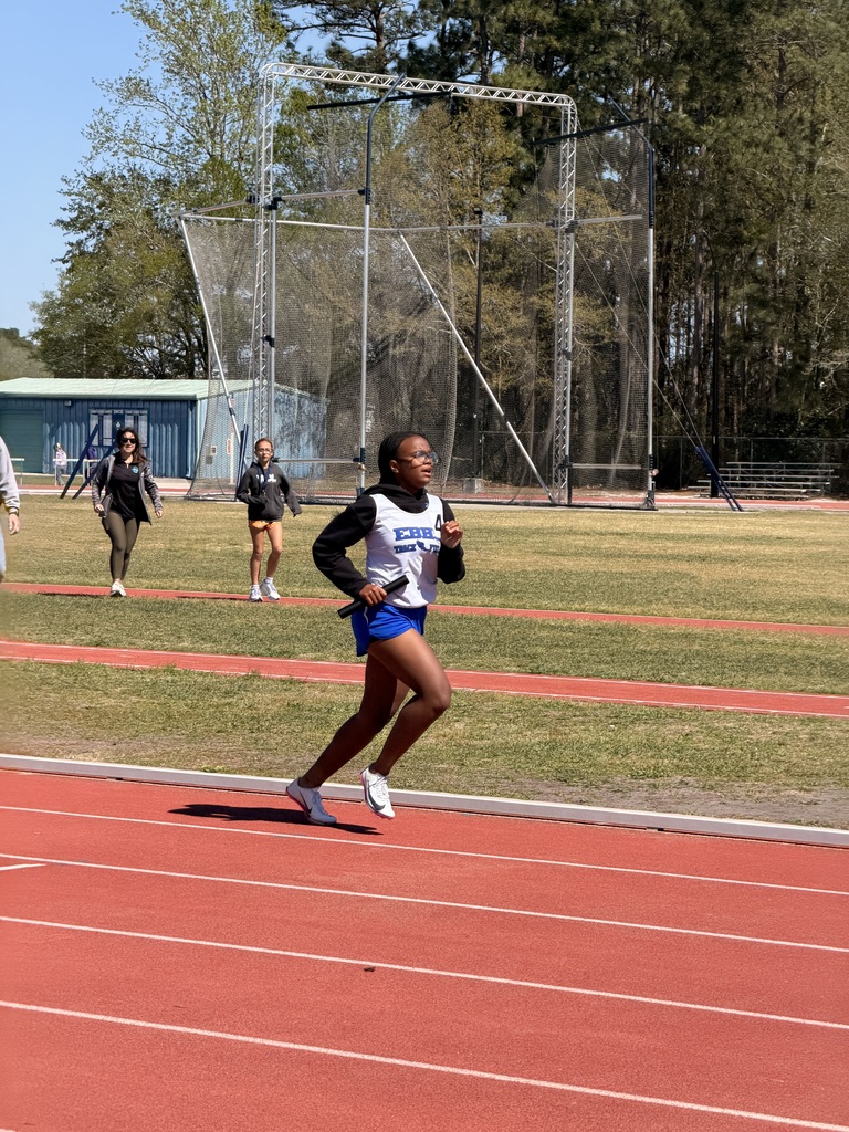 Female student in track uniform running on a track with a baton in their hand.