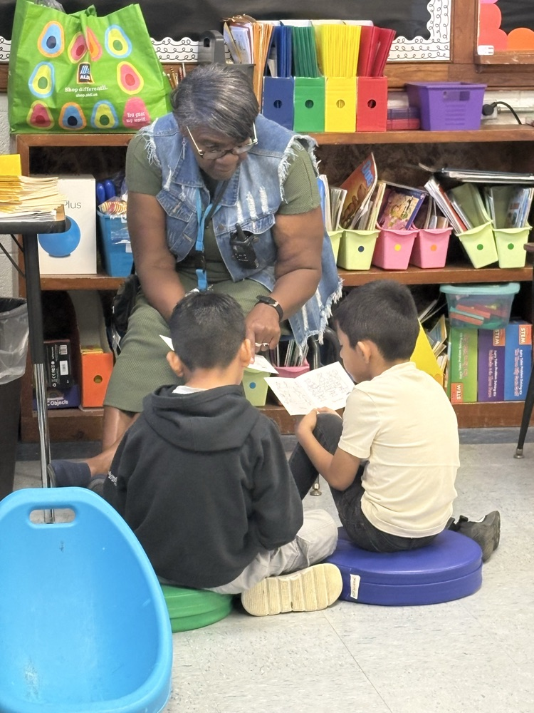 Two students sit together reading small books, focused on their literacy center work.