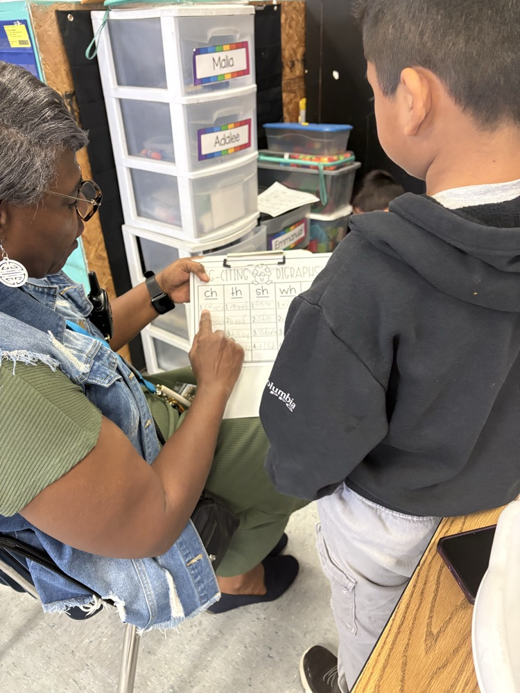 Two students sit together reading small books, focused on their literacy center work.