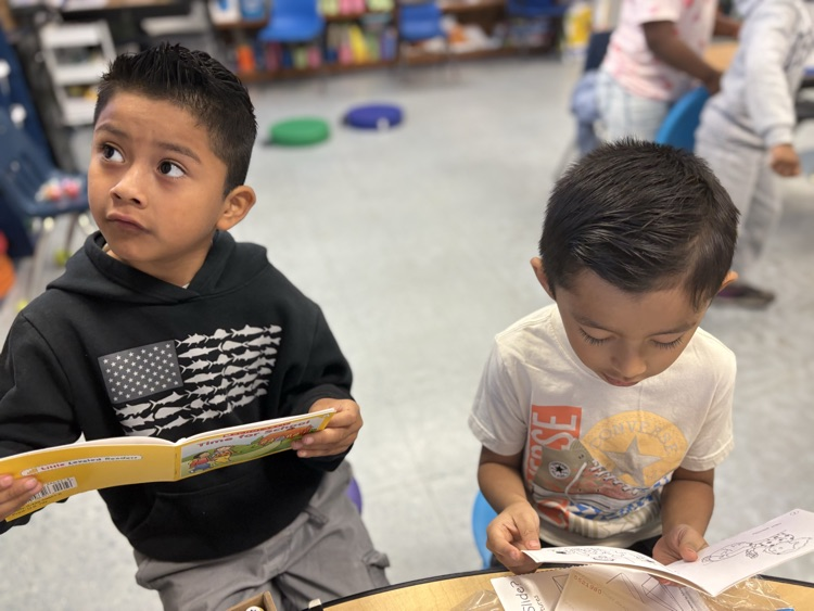 Two students sit together reading small books, focused on their literacy center work.