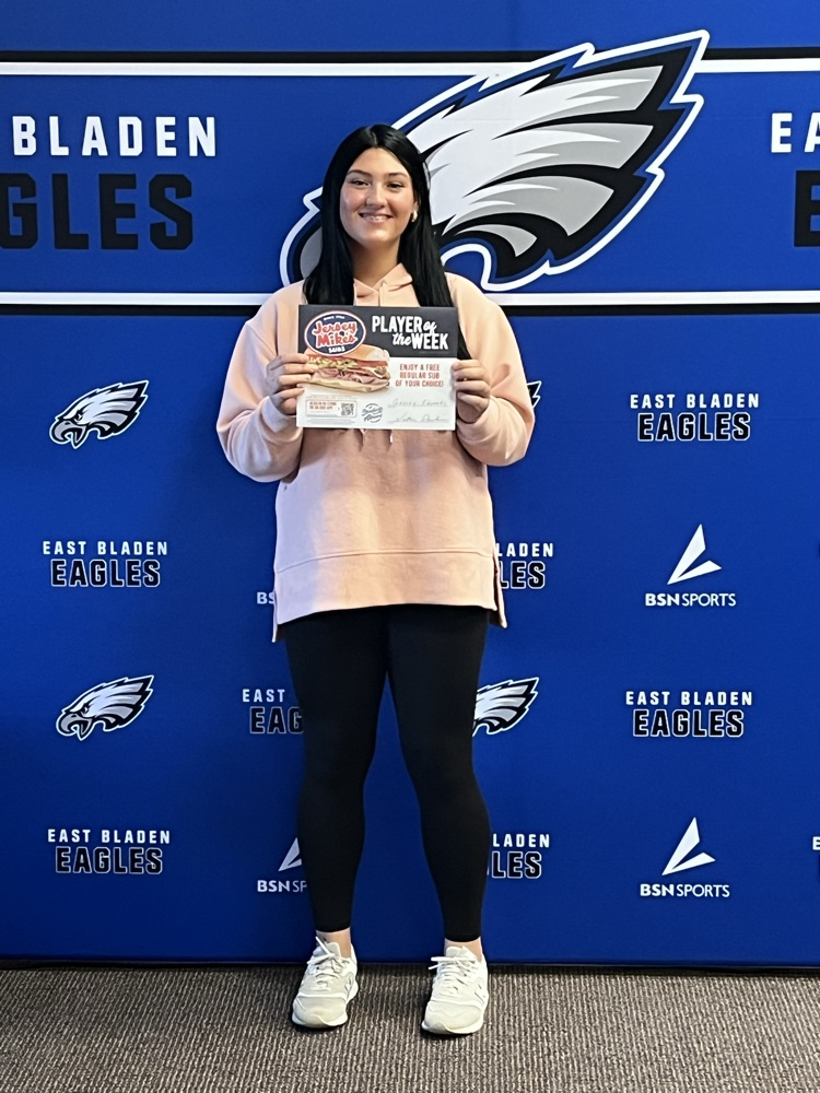 Blue background with East Bladen eagle girl and black leggings, pink top holding jersey Mike’s sign