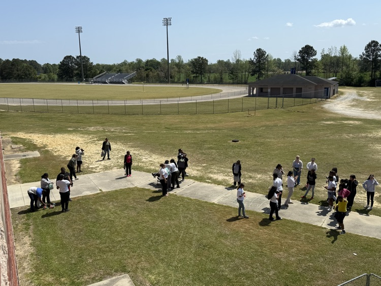 Students and teachers hunting easter eggs in the grass and playing on the sidewalk playing with chalk.