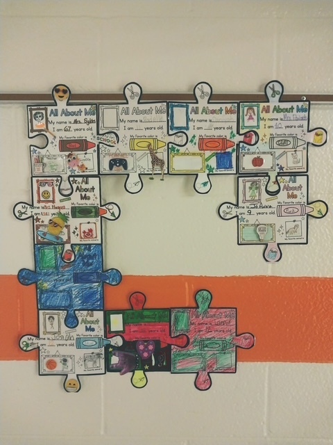 Student-created “All About Me” puzzle pieces are displayed on a wall, each filled with drawings and personal details, connected to form a large collaborative puzzle.