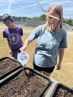 Student in blue shirt smiling and getting ready to water the squash