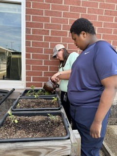 teacher in hat helping student water the plants