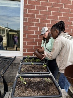 teacher in hat helping student water the plants