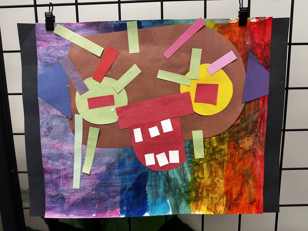 Child's mixed media collage of a monster face using cut paper shapes on a painted rainbow background