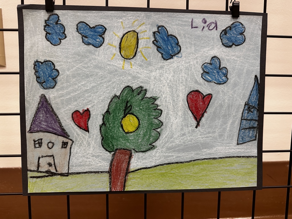 Child's crayon drawing of a landscape with a house, tree, hearts, clouds, and sun, signed "Lia"