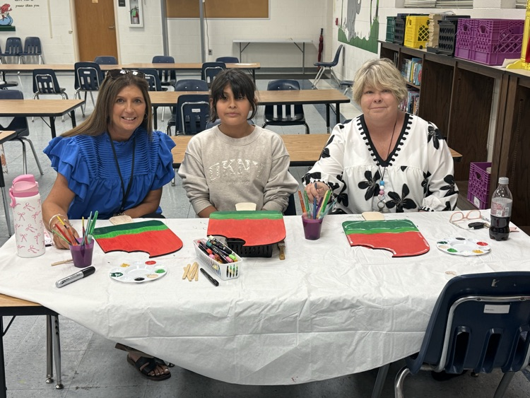 A group of participants sit closely together painting watermelon designs, focusing on adding details with brushes and paint.