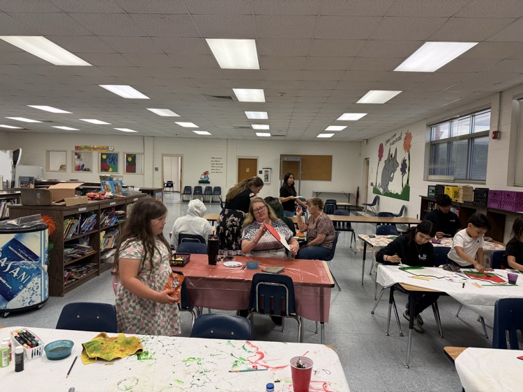 A group of participants sit closely together painting watermelon designs, focusing on adding details with brushes and paint.