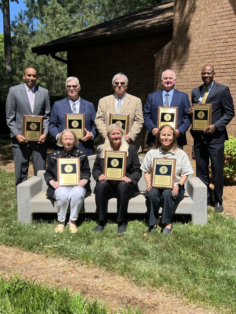 FIVE MEN STANDING IN THE BACK THREE WOMEN IN THE FRONT HOLDING THEIR HALL OF FAME PLAQUES, AND VERY GREEN GRASS