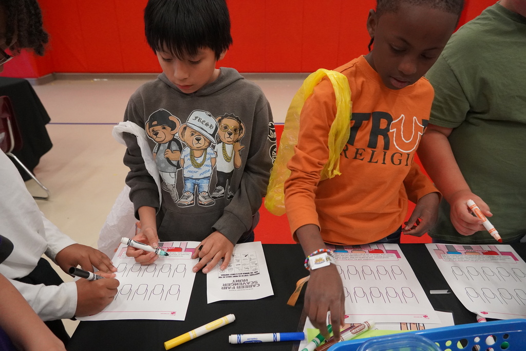 Two students are using markers to color in nail designs. 