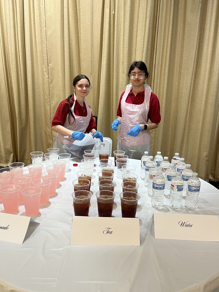two students serving drinks wearing white plastic aprons and gloves