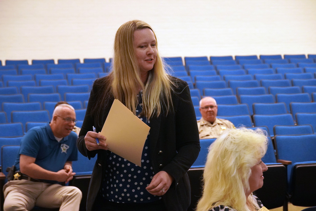 A female staff member is speaking to a group of adults. There is blue auditorium seating behind her. 