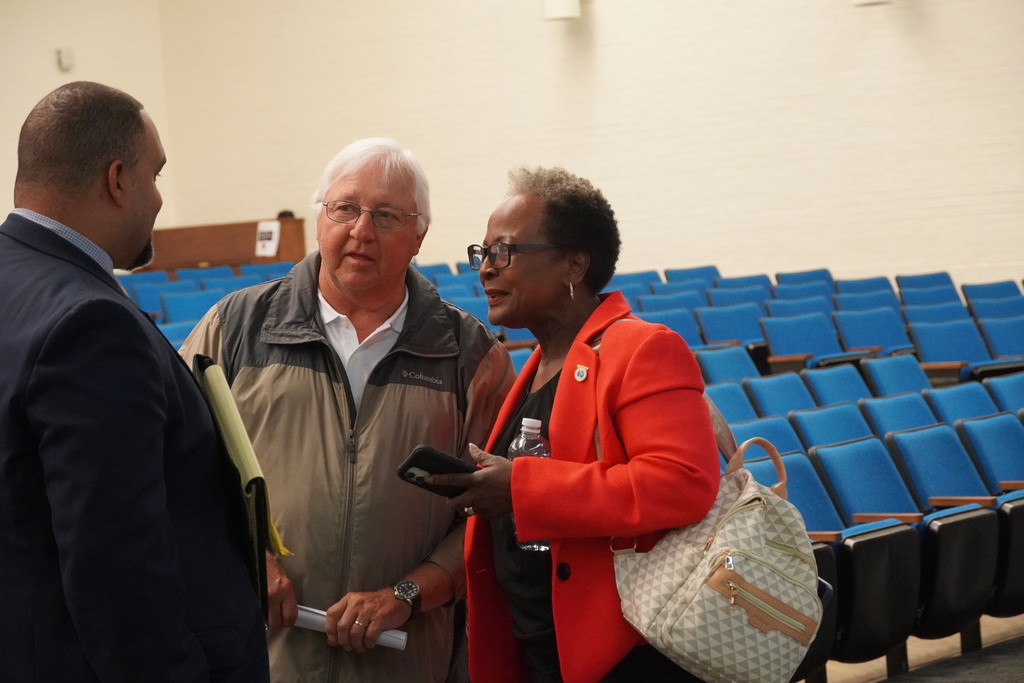 Three adults, two men and a woman stand together talking. 